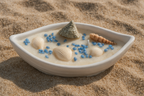 Déjate llevar por la calma del mar con esta vela artesanal presentada en un delicado recipiente de yeso cerámico con forma de barca.